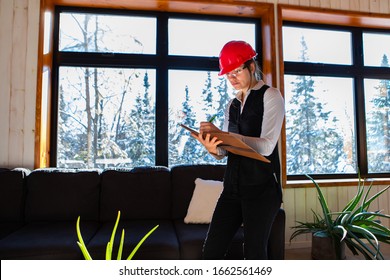 Home Inspector Woman Wearing Red Hard Hat Takes Professional Notes On Her Clipboard During Air Quality Inspection. House Interior With Indoor Plants.