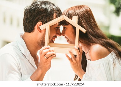 Home insurance concept. Young couple hold wooden home model in hands means they are planning about home insurance.
