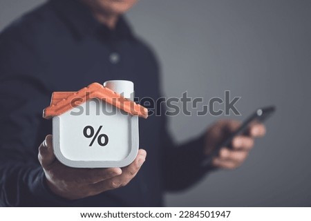 Home interest and financial concept, Money loan for housing idea, Real estate or Property management business concept, Man in black shirt holding grey wooden house model on dark backdrop. Studio shot.