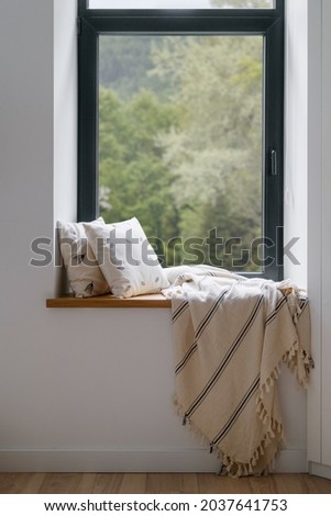 Home interior, cozy house room with blanket at window. Modern hygge design of relax place at windowsill, pillow decor for rest indoor. Nobody at comfortable sill with natural background.