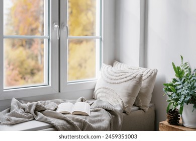 Home interior with cozy leisure area beside window with view on nature in autumn. Windowsill with blanket, cushions and paper book in scandinavian style room. Enjoy weekend morning. - Powered by Shutterstock