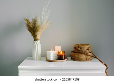 Home interior decor in beige neutral colors. White dresser with dried flowers in vase, rattan bags and candle. Still life, hygge concept. Selective focus