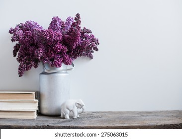 Home interior decor, bouquet of lilacs in a vase and books on rustic wooden table, on a white wall background