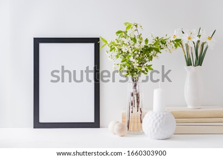 Home interior with decor elements. Mockup with a black frame, spring flowers in a vase on a light background