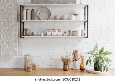 Inneneinrichtung, Nahaufnahme der weißen Küche. Modernes Dekor des skandinavischen Hauses, Holzregal mit dekorativem Keramikgeschirr. Rustikale Glasdetails bei Tischmöbeln.