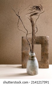 Home interior. Dry twigs branch composition in grey handcrafted ceramic vase standing on table with old wooden frame. Brown wall behind. Copy space.