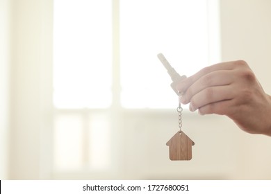 Home key in hand in apartment on empty room background inside new house. Real estate and moving concept