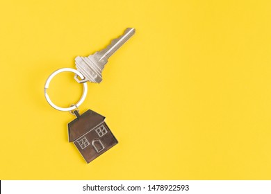 Home key with house keyring or keychain on solid yellow background using as home ownership, mortgage or buy and sell property and real estate.