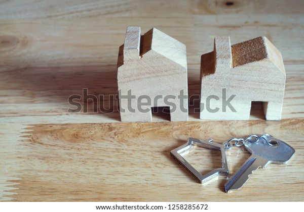 Home key with home\
keyring and wooden house model on bright background, real estate\
concept, copy space