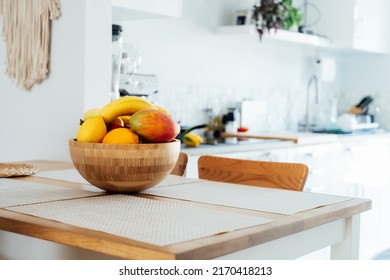 Home kitchen counter table with selective focus on bamboo bowl with exotic fruits on it with blurred background of modern cozy white kitchen. Home interior design details. Copy space. - Powered by Shutterstock