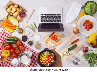 Home kitchen table top view with laptop, food ingredients, raw vegetables, kitchenware and utensils, top view - Powered by Shutterstock