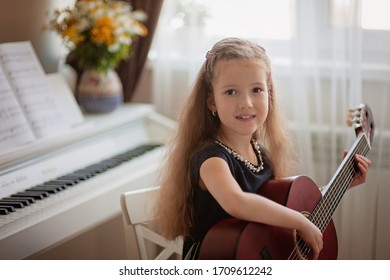 Home Lesson On Music For A Girl With A Guitar And Piano. The Idea Of Activities For The Child At Home During Quarantine