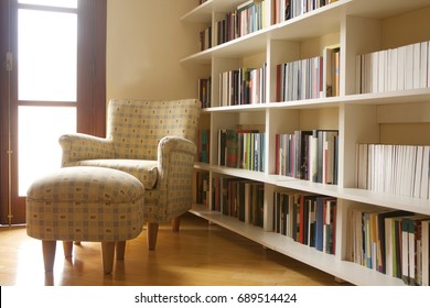 Home library with arm chair. Clean and modern decoration. Light coming from the window.
