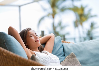 Home lifestyle woman relaxing sleeping on sofa on outdoor patio living room. Happy lady lying down on comfortable pillows taking a nap for wellness and health. Tropical vacation.