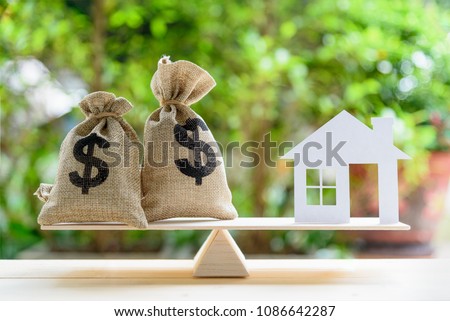 Home loan / reverse mortgage or transforming assets into cash concept : House paper model , US dollar hessian bags on a wood balance scale, depicts a homeowner or a borrower turns properties into cash