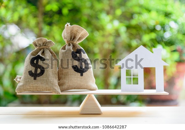 Home loan / reverse mortgage or transforming assets\
into cash concept : House paper model , US dollar hessian bags on a\
wood balance scale, depicts a homeowner or a borrower turns\
properties into cash