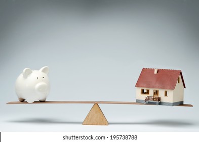 Home loans market. Model house and piggy bank balancing on a seesaw