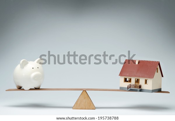 Home loans market. Model house and piggy bank\
balancing on a seesaw