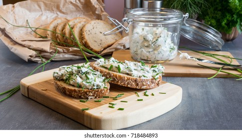 Home made bread on a wooden cutting board with curd cheese and ricotta and herbs. Decorated with green herbs 