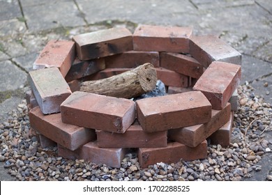 Home made brick built fire pit or barbecue with logs standing on coarse gravel on patio slabs