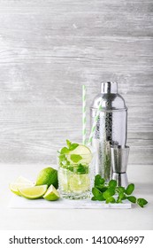 Home Made Mojito Cocktail Decorated With Lime, Mint Leaves, Ice Cubes And Silver Shaker Over White Bright Background