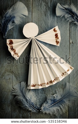 Home made paper angel surrounded by feathers  on blue wooden background.