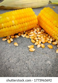Home made Sweet corn broken in half with scattered unpopped popcorn grains. Isolated on grey background.