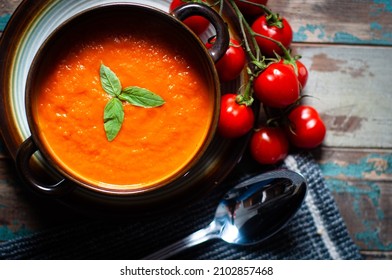 Home made tomato soup served on a rustic wooden table garnished with basil and vine ripened tomatoes.