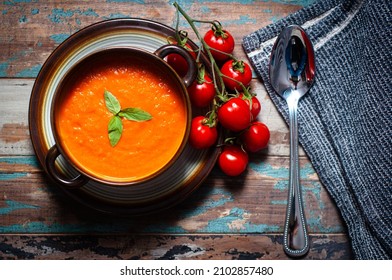Home made tomato soup served on a rustic wooden table garnished with basil and vine ripened tomatoes.
