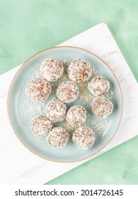 Home Made Vegan Energy Protein Balls With Coconut Flakes, Almond Butter, Oats, Nuts, Dates, Dried Fruit, Flax And Hemp Seeds Served On White Wooden Board.