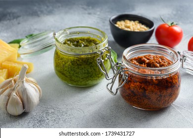 Home made Vegan pesto normal pesto and Red pesto and cooking ingredients Parmesan cheese, basil leaves, pine nuts, olive oil, garlic, salt, pepper side view on grey concrete surface close up - Powered by Shutterstock