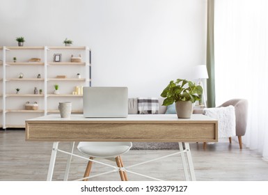 Home Manager, Freelance And Remote Worker At Home. Couch With Pillows, Table With Laptop And Cup Of Tea, Plant In Pot, Smartphone And Notebook, Shelves, Armchair, Gray Wall In Living Room Interior