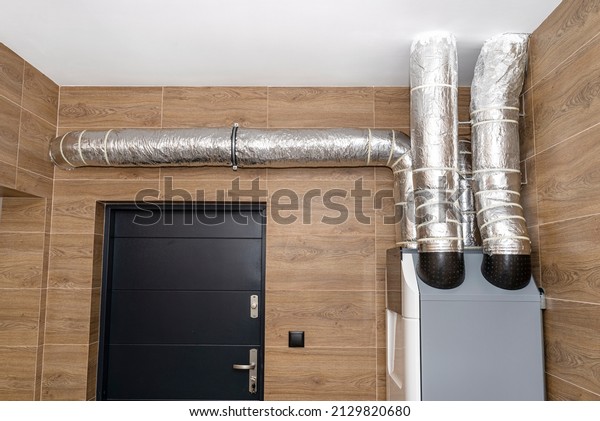 Home mechanical ventilation with heat recovery
hanging on the wall in a modern gas boiler room with brown ceramic
tiles imitating wood.