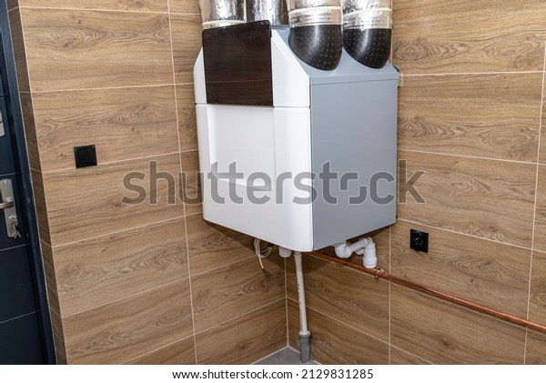 Home mechanical ventilation with heat recovery\
hanging on the wall in a modern gas boiler room with brown ceramic\
tiles imitating wood.