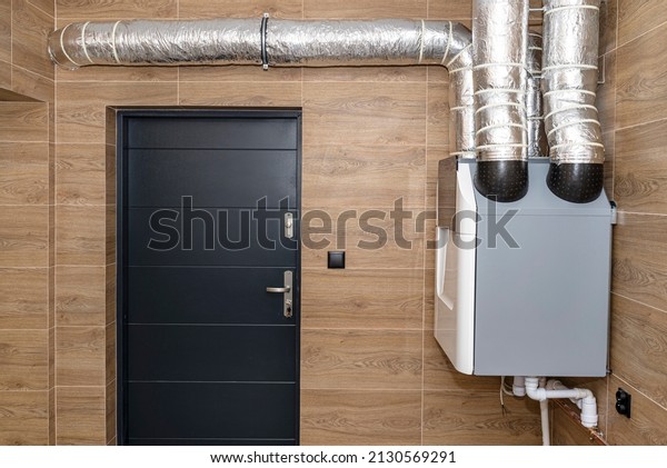 Home mechanical ventilation with heat recovery\
hanging on the wall in a modern gas boiler room with brown ceramic\
tiles imitating wood.