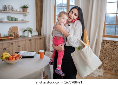 At Home. Mom Holding Daughter And Shopping Bag, Talking On The Phone, Smiling