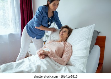 Home Nurse Making Elderly Patient Bed. Female Caregiver Adjusting Pillow For Senior Woman Lying In Hospital Bed.