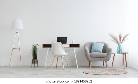 Home Office, Cabinet Or Workplace At House For Remote Work. Desk With Laptop, White Chair, Simple Armchair With Blue Pillow And Table With Vase And Dry Plants. Light Walls In Daylight, Panorama