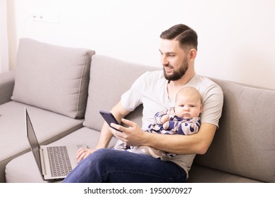 Home Office With Child. Beautiful Young Dad With Beard Working At Home With A Laptop And Smartphone While Sitting On The Couch With A Baby. Stay At Home, Online Shopping, Distance Work Concept. Indoor