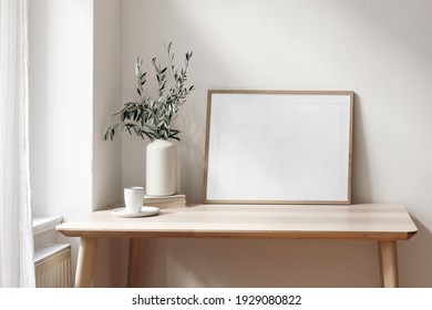 Home office concept. Empty horizontal wooden picture frame mockup. Cup of coffee on wooden table. White wall background. Vase with olive branches. Elegant working space. Scandinavian interior design. - Shutterstock ID 1929080822