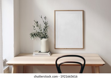 Home Office Concept. Old Books, Empty Vertical Wooden Picture Frame Mockup Hanging On White Wall. Wooden Desk, Table. Vase With Olive Branches. Elegant Working Space. Scandinavian Interior Design.