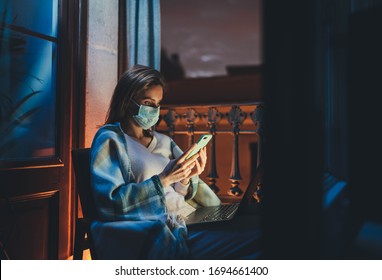 Home Office Concept, Young woman in fase mask working remotely from home using laptop computer at night, sick woman in medical mask having video conference with family or friends during quarantine  - Powered by Shutterstock