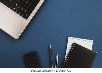 Schreibtisch des Hauses. Laptop, mobil, Taschenbuch und Stift auf dunkelblauem Hintergrund. Stilvoller Arbeitsbereich. Draufsicht, flache Lage, Kopienraum