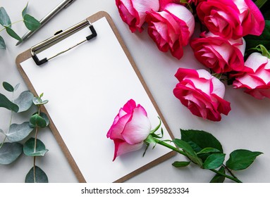 Home Office Desk Workspace With Blank Paper Clipboard, Red Roses Bouquet On White  Background. Flatlay