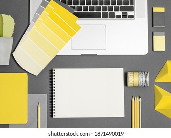 Home office for freelance girl. Bloggers workplace with illuminating yellow color samples, blank note, office supplies on ultimate gray backdrop. Mockup for text, sketch. Main colour of the year 2021