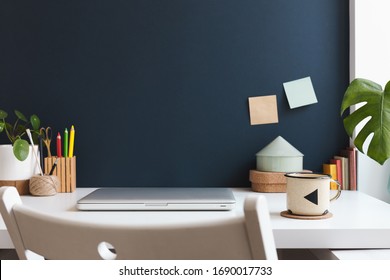 Home Office With Laptop Closed, Office Supplies, Mug, Notes, Books And Dark Blue Wall. Homeschooling Concept. Trendy, Creative Workspace.