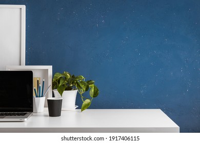 Home Office With Laptop In The Corner, Office Supplies, Mug With Tools, Notes, Books And Dark Blue
 Wall. Homeschooling Concept. Trendy, Creative Workspace.