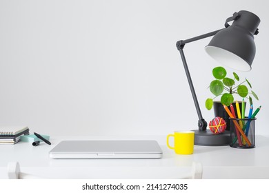 Home office with laptop stationery, laptop closed, books, design lamp near whie wall empty space. Working or learning from home concept. Stylish creative desk.