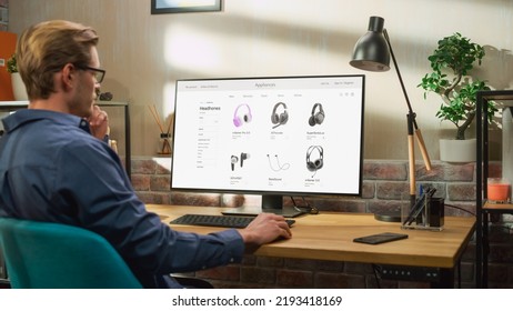 At Home Office: Man Using Desktop Computer, Online Shopping for Electronics, Wireless Hi-Fi Headphones. e-Commerce Concept of Purchasing, Buying, Ordering Tech Devices on Website. Over Shoulder View