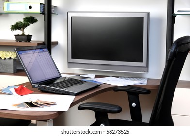 A Home Office With Open Laptop Desk Executive Chair Large TV And Work Set Out.